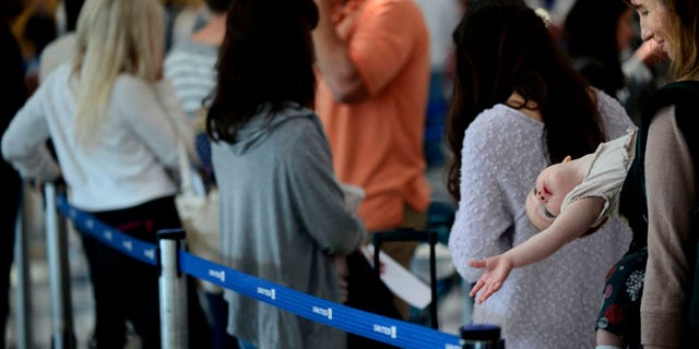 September 26, 2014: Ann Walden and her 15 month-old daughter Delphine wait in line after their flight to Baton Rouge was delayed at O'Hare International Airport in Chicago. All flights in and out of Chicago's two airports were halted Friday after a fire at a suburban air traffic control facility sent delays and cancellations rippling through the U.S. air travel network. (AP Photo/Paul Beaty)