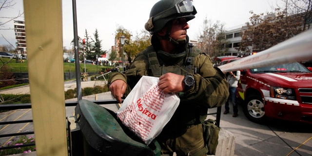 A police explosives expert inspects a garbage container near a blast site n Santiago, Chile, Monday Sept. 8, 2014.