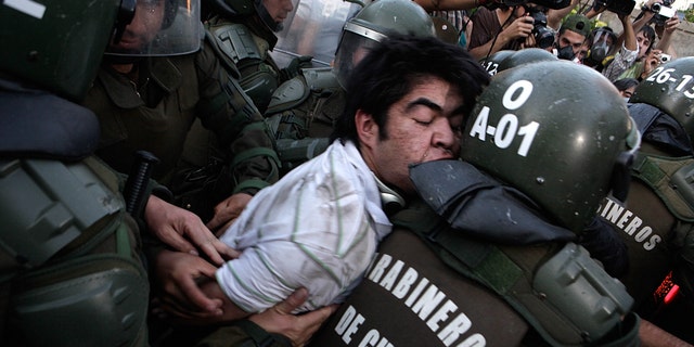 Police officers detain a human rights activist after clashes during an event honoring  Miguel Krassnoff, a former Chilean army brigadier during the 1973-1990 dictatorship of August Pinochet, in Santiago, Chile, Monday, Nov. 21, 2011. Krassnoff is currently serving a 144-year sentence for homicide and forced disappearances.  (AP Photo/Luis Hidalgo)