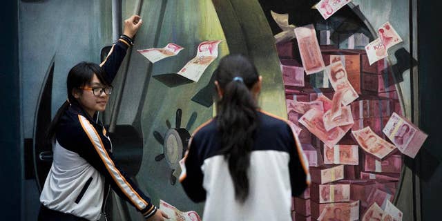 A woman takes a souvenir photo for her friend posing with a 3-D painting of a vault loaded with piles of 100 Chinese yuan (US$16.17) notes at a shopping mall in Beijing, China Friday, May 22, 2015. Negotiators from 57 governments completed work Friday on a charter for a Chinese-led Asian regional bank and it is due to be signed in late June, the Chinese finance ministry said. (AP Photo/Andy Wong)