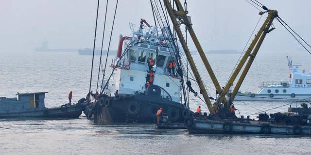 In this photo released by China's Xinhua News Agency, rescuers approach the lifted wreckage of capsized tug boat "Wanshenzhou 67" on the Yangtze River near Jingjiang, east China's Jiangsu Province, Saturday, Jan. 17, 2015. Authorities confirmed 21 people dead in the capsizing of the tugboat with an international team on a test voyage in eastern China, after rescuers dragged the overturned vessel to shallow waters and scoured it Saturday. (AP Photo/Xinhua, Shen Peng) NO SALES