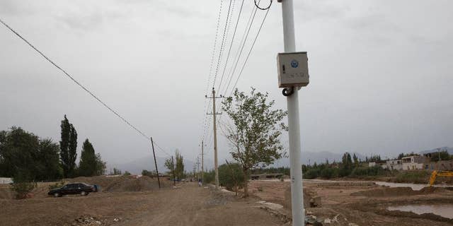 In this photo taken Wednesday, July 16, 2014, a child plays under police surveillance cameras set up to monitor a dirt road intersection in Kuqa in western China's Xinjiang province. (AP Photo/Ng Han Guan)