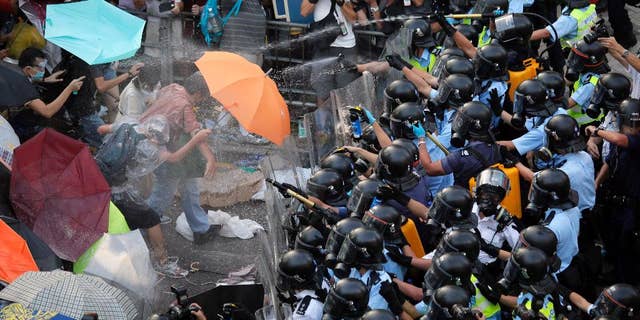 FILE - In this Sept. 28, 2014 file photo, riot police use pepper spray against protesters after thousands of people block a main road to the financial central district outside the government headquarters in Hong Kong. Ubiquitous images in Hong Kong media with masses of unarmed students fending off pepper spray with umbrellas could not contrast more starkly with mainland China’s virtual blackout of news about the territory’s pro-democracy protests. (AP Photo/Vincent Yu, File)
