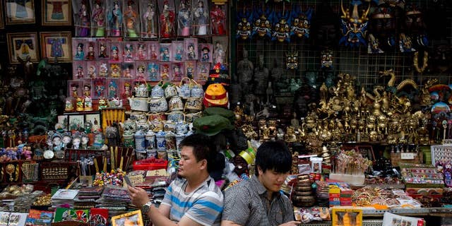 Vendors browse their smartphones as they wait for customer at their store selling Chinese made souvenirs at the Wangfujing shopping district in Beijing, China Thursday, May 21, 2015. Manufacturing in China shrank for the third straight month in May as demand remained soft, raising the chances of more stimulus to prop up growth in the world's No. 2 economy. (AP Photo/Andy Wong)