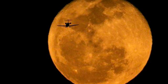 A jet is silhouetted by the rising waning moon on a landing approach at Phoenix's Sky Harbor International Airport on March 6, 2015.