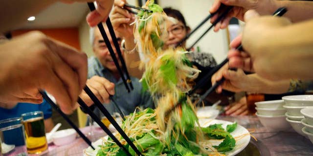 In this photo taken on Monday, Feb. 16, 2015, Cheong Lan Yang, 68, rear left, tosses "yu sheng," a raw fish salad, with family members during a family reunion dinner for Chinese New Year, at a restaurant in Singapore. This Singaporean tradition is known as “lo hei,” which means “tossing up good fortune” in Cantonese and is done at the start of family reunion dinners before Chinese New Year. The raw fish in the salad symbolizes the abundance of wealth and long life that Cheong, who lives in Australia, hopes for in the new year. “I hope this Chinese New Year brings good health because I would like to live long enough to see my grandchildren one day,” he said. “Chinese New Year is a time for family gathering and that means a lot to me because I currently live abroad, and this is a time for us to share old memories as well as make new ones.” (AP Photo/Wong Maye-E)