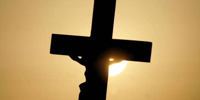 FILE -- A cross is silhouetted against the sun outside the Woodside Hospice in Pinellas Park, Fla.