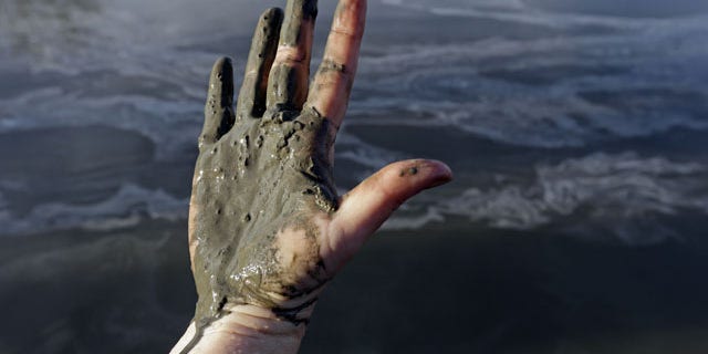 February 5, 2014: Amy Adams, North Carolina campaign coordinator with Appalachian Voices, shows her hand covered with wet coal ash from the Dan River swirling in the background as state and federal environmental officials continued their investigations of a spill of coal ash into the river in Danville, Va. Duke Energy estimates that up to 82,000 tons of ash has been released from a break in a 48-inch storm water pipe at the Dan River Power Plant in Eden N.C. on Sunday. (AP Photo/Gerry Broome)