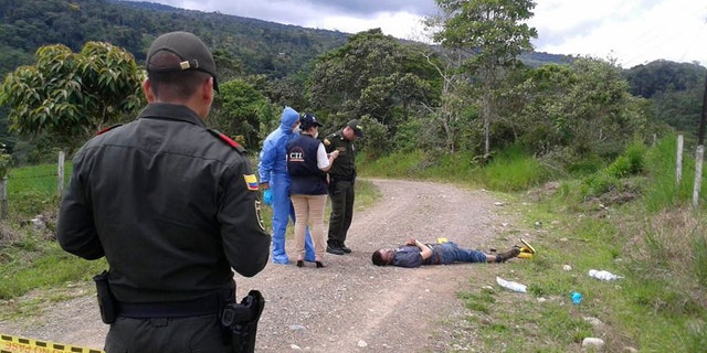 In this photo taken Wednesday, April 23, 2014, police officers and forensics look at the body of British citizen Henry Miller, 19, on a road outside Mocoa, in Colombia's southwestern state of Putumayo. Miller died after he drank a hallucinogen during a tribal ritual, his body left by the side of the road by two frightened young local men, said Saturday local police commander Ricardo Suarez. (AP Photo/Jose Horacio Villarreal)