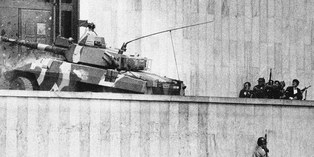 FILE - In this Nov. 6, 1985, file photo, an armored vehicle crashes through the two story wooden doors at the front entrance to the Palace of Justice in Bogota, as soldiers and policemen prepared to rush inside. The Inter-American Court of Human Rights has charged Colombia, Wednesday Dec. 10, 2014, with human rights violations in connection with the disappearance of 10 people in 1985’s hostage crisis at the Supreme Court. The court ordered Colombia to provide relatives with compensation and psychological assistance, publish its sentence in national news media, and continue investigating the case. In addition to those disappeared, more than 100 people were killed in the government operation to retake the building, including all rebels and many judges. (AP Photo/Carlos Gonzalez, File)