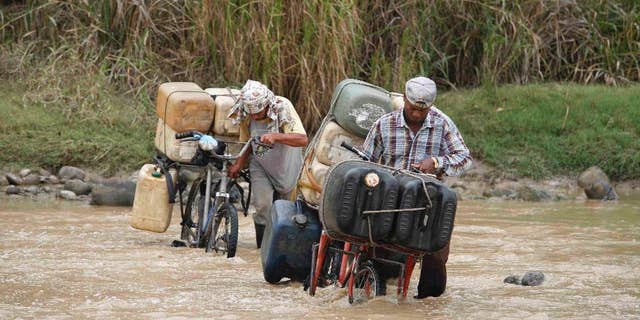 FILE - In this March 7, 2008 file photo, smugglers cross the Tachira River carrying Venezuela gasoline into Colombia, in Cucuta, at the Colombian border with Venezuela. President Nicolas Maduro has ordered the closure of a major border crossing with Colombia after three soldiers were attacked while looking for smugglers. Maduro late Wednesday, Aug. 19, 2015, said the normally busy border in western Tachira state would remain closed for 72 hours. (AP Photo/William Fernando Martinez, File)