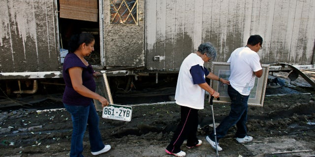 In this Sept. 24, 2013, photo, resident Mari Partida, left, walks with the plate from her destroyed car, as her neighbor Sofia Mendez leans on her son for support as he carries a painting recovered from their trailer, one of the many homes now declared uninhabitable due to permanent flood damage at a trailer park in Evans, Colo. Many undocumented immigrants working in the U.S. have returned to their mobile home parks in flood-ravaged Colorado to find that there was little left to salvage. Like many in the stricken region, they didnt have flood insurance. And because many are not citizens or legal residents, they cant get government help. (AP Photo/Brennan Linsley)