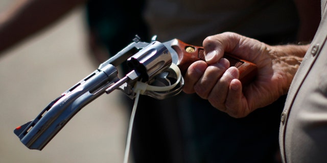 FILE: July 30, 2013: A deputy sheriff looks at a disabled gun to be melted down at a gun buy-back program in Los Angeles, Calif.