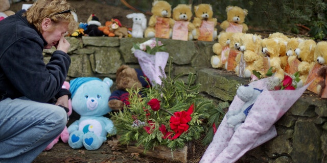 Cheryl Girardi, of Middletown, Conn., kneels beside 26 teddy bears, each representing a victim of the Sandy Hook Elementary School shooting, at a sidewalk memorial, Sunday, Dec. 16, 2012, in Newtown, Conn. A gunman walked into Sandy Hook Elementary School in Newtown Friday and opened fire, killing 26 people, including 20 children.(AP Photo/David Goldman)