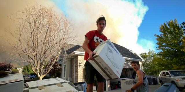 In this Thursday, Sept. 13, 2018, photo Brandon Morgan, 17, center, loads items into a truck as his friend, Carter Wilkey, 16, helps Morgan evacuate from his Elk Ridge, Utah home during a mandatory evacuation. A fast-moving Utah wildfire fanned by high-winds has more than doubled in size as it burns through dry terrain and forces evacuations of hundreds of homes, the U.S. Forest Service said Friday. (Isaac Hale/The Daily Herald via AP)