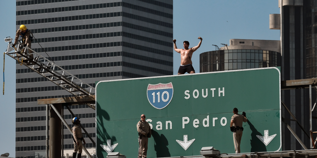 California Highway Patrol officers try to Alexander Dunn off off a freeway sign in downtown Los Angeles on June 27, 2018.