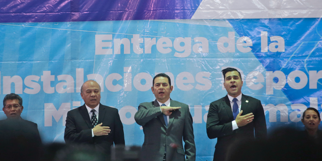 Guatemalan President Jimmy Morales, center, sings the national anthem, acompanied by Mixco mayor Ernesto Bran, right, and Culture Minister Jose Chex, during the inauguration of a soccer field in Mixco, Guatemala, Monday, Sept. 17, 2018. Morales' government will defy a ruling by the country's top court and block the return of Ivan Velasquez, who is leading a U.N.-backed anti-corruption commission. (AP Photo/Moises Castillo)