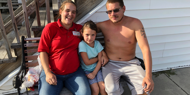 In this Wednesday, Sept. 12, 2018, Mercedes O'Neill, her 6-year-old daughter Sophieand boyfriend Kelly Johnson sit outside their home in North Myrtle Beach, S.C. O'Neill thought a long time about evacuating from Hurricane Florence but decided they couldn't afford it. (AP Photo/Jeffrey Collins)