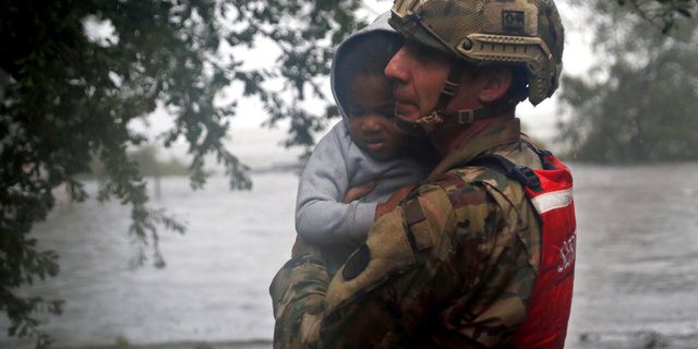 Rescue team member Sgt. Nick Muhar, from the North Carolina National Guard 1/120th battalion, evacuates a young child as the rising floodwaters from Hurricane Florence threatens his home in New Bern, N.C., on Friday, Sept. 14, 2018. (AP Photo/Chris Seward)