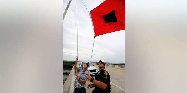 Isle of Palms Fire Chief Ann Graham, at left, and Isle of Palms police officer Thomas Molino III raise a tropical storm warning flag over the Isle of Palms Connector shortly after Charleston County, S.C., went under a tropical storm warning due to Hurricane Florence Thursday, Sept. 13, 2018, in Isle of Palms, S.C. (AP Photo/Mic Smith)