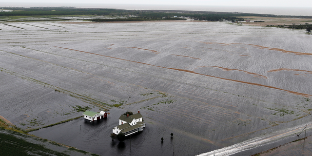 A pickup truck drives on a flooded road past a farm house that is surrounded by flooded fields from tropical storm Florence in Hyde County, NC., Saturday, Sept. 15, 2018. (AP Photo/Steve Helber)