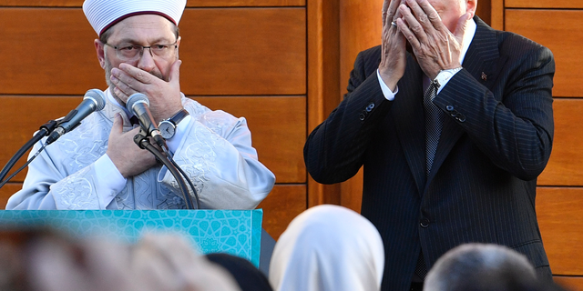 Turkish President Recep Tayyip Erdogan, right, and Diyanet President Ali Eras cover their faces during a prayer on occasion of the opening of the new mosque in Cologne, Germany, on Saturday, Sept. 29, 2018. (AP Photo/Martin Meissner)