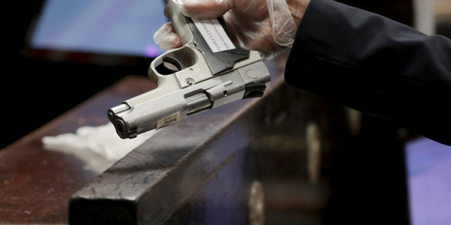 In this Tuesday Sept. 18, 2018 photo, Chicago Police Detective Roberto Garcia holds officer Jason Van Dyke's 9mm semiautomatic Smith and Wesson at the trial for the shooting death of Laquan McDonald at the Leighton Criminal Court Building in Chicago. Garcia was asked to confirm it was the gun Van Dyke turned in hours after the shooting that Van Dyke used to kill McDonald. (Antonio Perez/ Chicago Tribune via AP, Pool)