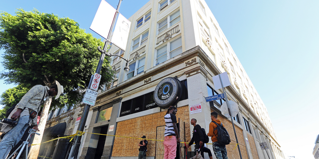 People who may have been occupants and others stand around a four-story vacant commercial building in Los Angeles' Hollywood district that was raided early in the morning of Wednesday, Sept. 12, 2018. Los Angeles police say more than 60 adults and at least four juveniles were detained during the raid where some people had been squatting. A search warrant was served before dawn on Hollywood Boulevard and officers went through the building, room by room, over several hours. Two firearms — a shotgun and a rifle— and drugs were seized, officials said. (AP Photo/Reed Saxon)