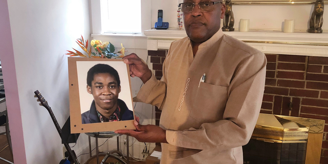 FILE - In this Sept. 5, 2018 file photo, Dia Khafra, father of Askia Khafra, holds a photo of his son in his Silver Springs, Md., home. The parents of 21-year-old Askia Khafra sued 27-year-old Daniel Beckwitt and his father on Monday, Sept. 10, 2018, the anniversary of the fire that killed Khafra in the basement of the Beckwitts' house in Bethesda, Maryland. (AP Photo/Michael Kunzelman)
