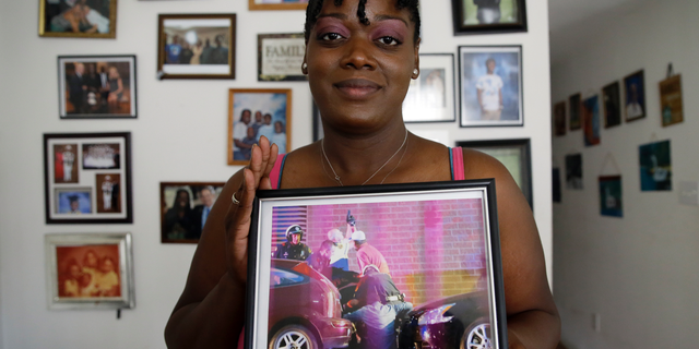 In this June 30, 2017, photo, Shetamia Taylor holds a picture that hangs on her living room wall in Garland, Texas, that shows first responders assisting Taylor after she was shot during a Black Lives Matter protest in downtown Dallas on July 7, 2016.