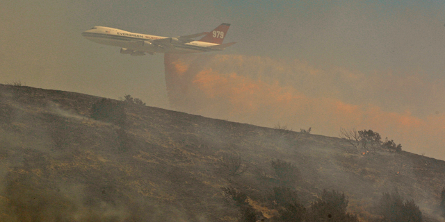 FILE - In this July 30, 2010, file photo, a Boeing Evergreen B-747 Supertanker drops fire retardant over a hillside subdivision on the outskirts of Palmdale, Calif. A report released Friday, Sept. 14, 2018, by California’s firefighting agency says firefighter Mathew Burchett was killed on Aug. 13, by a tree uprooted when thousands of gallons of flame-suppressing liquid were dropped from a similar Boeing 747 flying only 100 feet above the treetops at the Mendocino Complex fire north of San Francisco. (AP Photo/Damian Dovarganes, File)