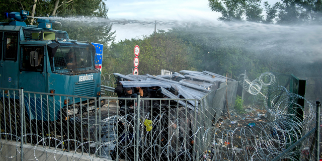 FILE - In this Sept. 16, 2015 file photo Hungarian police use water canons against refugees at the "Horgos 2" border crossing into Hungary, near Horgos, Serbia. A Hungarian appeals court on Thursday lowered to five years from seven the prison sentence of a Syrian man convicted of entering Hungary illegally and of complicity in throwing rocks at police during a 2015 border riot. The case stems from rioting at the Hungary-Serbia border on Sept. 16, 2015, when dozens of police officers, migrants and some journalists were injured in clashes a day after Hungary closed the frontier, stranding hundreds of migrants. (Tamas Soki/MTI via AP, file)