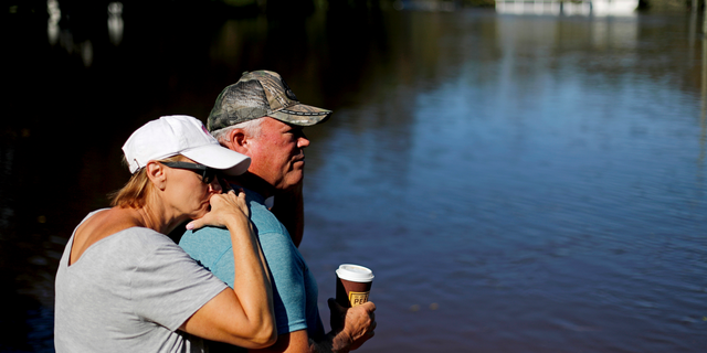 Dianna Wood, left, embraces her husband Lynn, as they look out over their flooded property as the Little River continues to rise in the aftermath of Hurricane Florence in Linden, N.C., Tuesday, Sept. 18, 2018. "I'm still hopeful," said Lynn about his home which currently has water up to the front step. "In another foot, I'll be heartbroken," he added. (AP Photo/David Goldman)