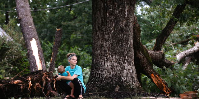 Sierra Price and son, Ryland Ross, 10 months, wait outside their home at Julian and Glendale Streets as work begins on cleanup in the area near Richmond,Virginia on Tuesday, Sept. 18, 2018, the day after Florence-spawned tornadoes caused damage and claimed one life in the area.( Joe Mahoney/Richmond Times-Dispatch via AP)