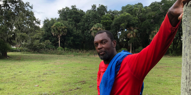 In this Sept. 11, 2018 photo, John Brown stands behind a fence for his cows outside his home on St. Helena Island, S.C. Brown and other residents of the island's Gullah community of slave descendants are watching Hurricane Florence as it approaches the Carolinas. St. Helena's Gullah residents have a long history of riding out storms, including a hurricane that killed an estimated 2,000 people in 1893. (AP Photo/Russ Bynum)