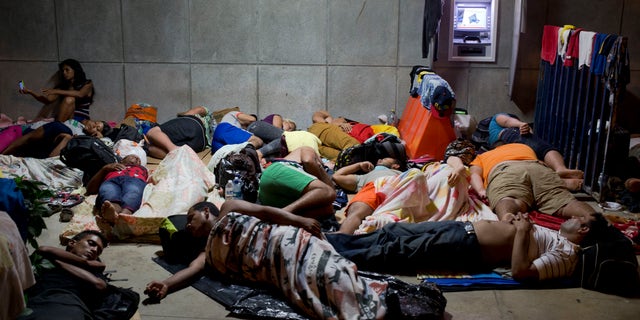 In this Saturday, Nov. 21, 2015 photo, a Cuban woman migrant uses her cell phone while other Cubans sleep, outside of the border control building in Penas Blancas, Costa Rica, on the border with Nicaragua. Some 45,000 Cubans will move by bus, boat, taxi and on foot from Ecuador and other South and Central American countries to the Texas and California borders this year, afraid that the normalization of relations between the U.S. and Cuba will mean an imminent end to special immigration privileges that date to the opening of the Cold War. (AP Photo/Esteban Felix)