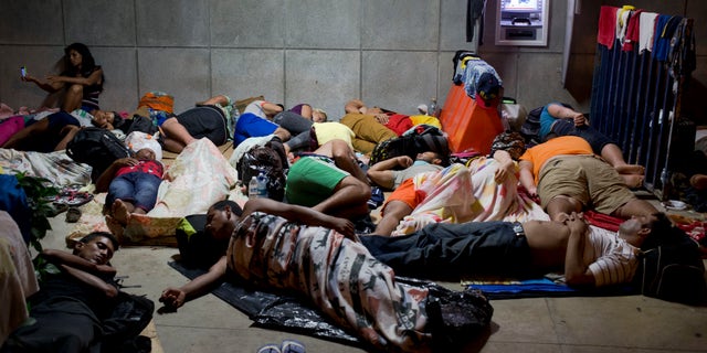 In this Saturday, Nov. 21, 2015 photo, a Cuban woman migrant uses her cell phone while other Cubans sleep, outside of the border control building in Penas Blancas, Costa Rica, on the border with Nicaragua. Some 45,000 Cubans will move by bus, boat, taxi and on foot from Ecuador and other South and Central American countries to the Texas and California borders this year, afraid that the normalization of relations between the U.S. and Cuba will mean an imminent end to special immigration privileges that date to the opening of the Cold War. (AP Photo/Esteban Felix)