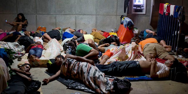 In this Nov. 21, 2015 file photo, a Cuban woman migrant uses her cell phone while other Cubans sleep, outside of the border control building in Penas Blancas, Costa Rica. (AP Photo/Esteban Felix, File)