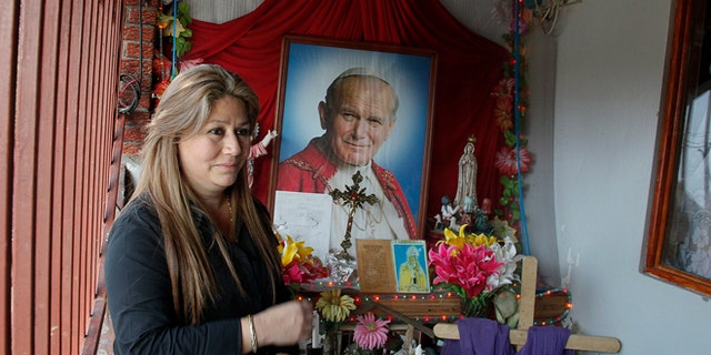 Costa Rica's Floribeth Mora stands by the shine she made to Pope John Paul II at the entrance to her home in La Union de Cartago, east of the capital of San Jose, Costa Rica, Friday, July 5, 2013. Pope Francis approved the miracle needed to canonize Pope John Paul II this morning at the Vatican. Floribeth Mora suffered from a cerebral aneurysm that was inexplicably cured on May 1, 2011, the date of John Paul's beatification, when people filled St. Peter's Square to honor the beloved Polish pontiff. (AP Photo/Enrique Martinez)