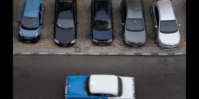 A vintage automobile drives by a parking lot of modern vehicles in Havana, Cuba, Thursday, Dec. 19, 2013. According to official media the government is opening the automobile market by eliminating the special permit that strictly limited the number of people allowed to buy vehicles from the state. (AP Photo/Franklin Reyes)