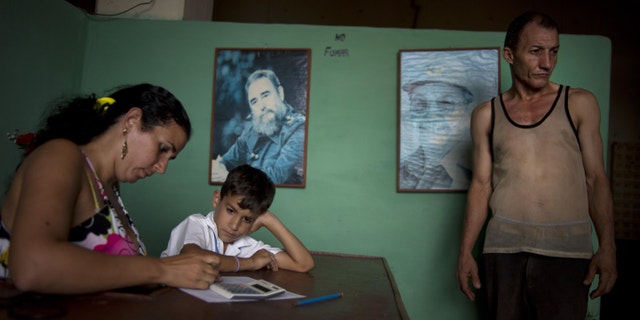 A worker, right, leaves the tobacco factory as a child waits for his mother to finish at a warehouse in the western province of Pinar del Rio, Cuba, Tuesday, Feb. 25, 2014. Pictures of Cuba's Fidel Castro and Raul Castro hang on the wall. Cigar enthusiasts from around the world come to Cuba during the annual Cigar Festival to visit tobacco farms and factories and savor new cigar brands. (AP Photo/Ramon Espinosa)