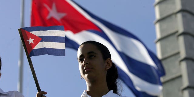 HAVANA, CUBA - DECEMBER 02: A young women waves a Cuban flag in Havana's Revolution Square during the 50th anniversary celebration of the forming of Cuba's Revolutionary Armed Forces December 2, 2006 in Havana, Cuba. Many in the crowd were hoping to catch a glimpse of Cuban President Fidel Castro who did not attend the parade. (Photo by Joe Raedle/Getty Images)