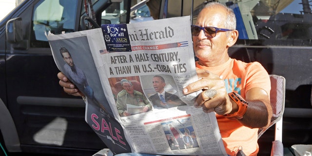 MSNBC photographer Tony Zumbado reads the Miami Herald in the Little Havana area of Miami, Thursday, Dec. 18, 2014, as news agencies from all over the world prepare to cover the reaction of the Cuban-Americans to the surprising move by President Barack Obama to restore the nation's ties with Cuba. The U.S. and Cuba will begin taking steps to restore full diplomatic relations, marking the most significant shift in U.S. policy toward the communist island in more than half a century. (AP Photo/Alan Diaz)