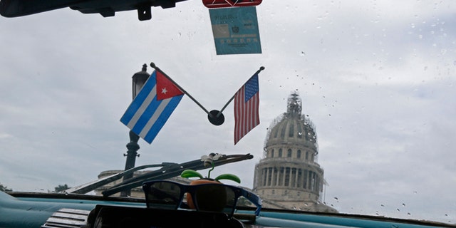 A Cuban and U.S. miniature national flags decorate the inside of a classic American car used as a collective taxi passes the Capitol Building in Havana, Cuba, Friday, Jan. 16, 2015. Tens of thousands more American tourists are expected to flock this year to a country where some five-star hotels don't have working air-conditioning or hand towels. The Obama administration hopes the new wave of U.S. tourists will fuel one of the healthiest parts of Cuba's new entrepreneurial sector, the thousands of private bed and breakfasts. (AP Photo/Desmond Boylan)