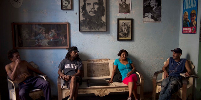 Roberto Alvarez, 47, right, chats with friends backdropped by a wall decorated with images of Cuban revolutionary heroes, Che Guevara, Fidel Castro and his brother, President Raul Castro, in Havana, Cuba, Wednesday, Feb. 25, 2015. Any kind of benefit for the Cuban people, thatll be hard. said Alvarez when asked if the negotiations with the US would help. (AP Photo/Ramon Espinosa)