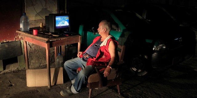 Andres Ortega, who works parking cars, is illuminated by an arriving car as he watches a baseball game between the Atlanta Braves and Washington Nationals that was played in May, on state television in Havana, Cuba, late Sunday, June 30, 2013. Cubans got a rare treat when state TV carried a Major League Baseball game for the first time in more than 50 years, but expressed disappointment when it turned out to be a nearly two-month old match-up without any of the defected Cuban stars whom islanders are most eager to follow. (AP Photo/Franklin Reyes)
