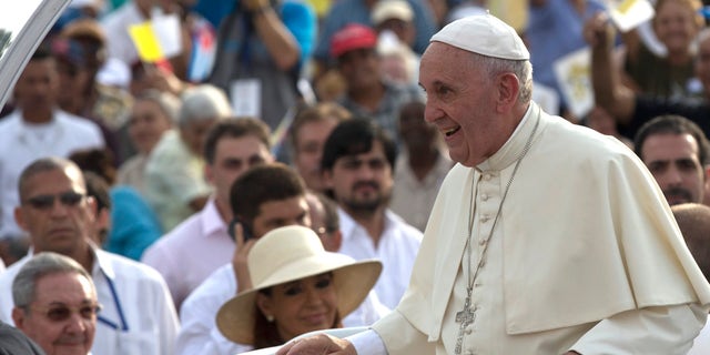 Cuba's President Raul Castro, behind left, and Argentina's President Christina Fernandez, in hat, watch Pope Francis arrive for Mass at Revolution Plaza in Havana, Cuba, Sunday, Sept. 20, 2015.  Pope Francis opens his first full day in Cuba on Sunday with what normally would be the culminating highlight of a papal visit: Mass before hundreds of thousands of people in Havana's Revolution Plaza. (Ismael Francisco/Cubadebate Via AP)