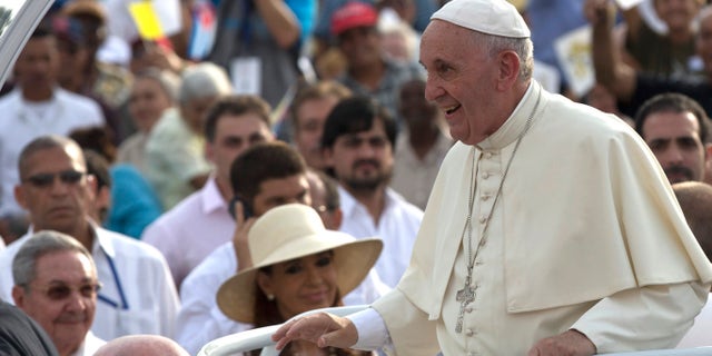 Cuba's President Raul Castro, behind left, and Argentina's President Christina Fernandez, in hat, watch Pope Francis arrive for Mass at Revolution Plaza in Havana, Cuba, Sunday, Sept. 20, 2015. Pope Francis opens his first full day in Cuba on Sunday with what normally would be the culminating highlight of a papal visit: Mass before hundreds of thousands of people in Havana's Revolution Plaza. (Ismael Francisco/Cubadebate Via AP)