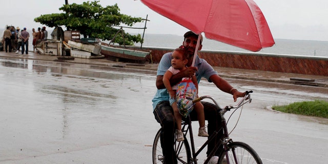 A man balances a child and umbrella on his bike as it rains during the approach of Hurricane Sandy in Manzanillo, Cuba, Wednesday, Oct. 24, 2012. Hurricane Sandy pounded Jamaica with heavy rain as it headed for landfall near the country's most populous city on a track that would carry it across the Caribbean island to Cuba, and a possible threat to Florida. (AP Photo/Franklin Reyes)