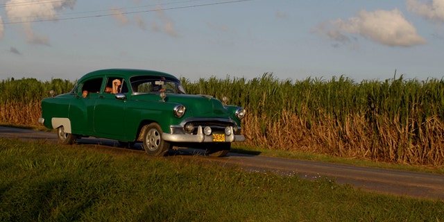 In this Sept. 8, 2012 photo, people drive a classic American car past a sugar cane field in Camaguey, Cuba. Just two years ago, Cuba's sugar industry was on its knees after the worst harvest in more than a century. Now Cuba's signature industry is showing signs of life. With world market prices rebounding, sugar is suddenly more profitable, and a reorganization of the sector could offer a blueprint for how to lift up the rest of the island's economy. (AP Photo/Franklin Reyes)
